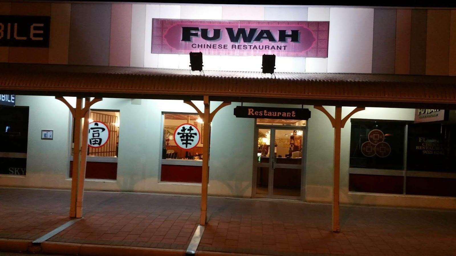 Fu Wah's shopfront at night on Wilson Street, Kalgoorlie, with its pink sign and red 富 華 window medallions